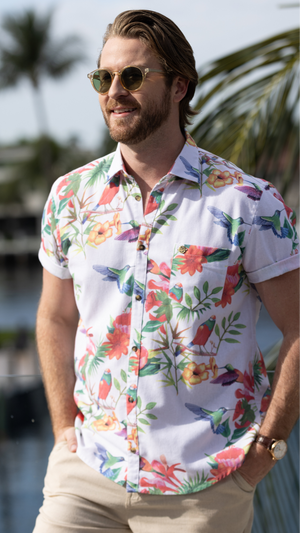 Man wearing a colorful floral shirt with sunglasses and palm trees in the background